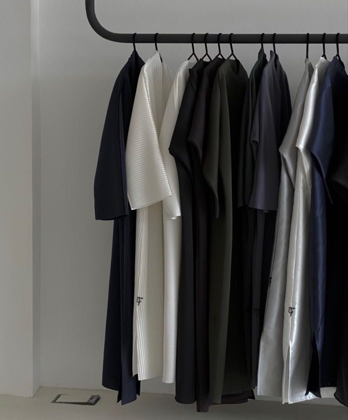 Clothing rack with various garments against a plain wall